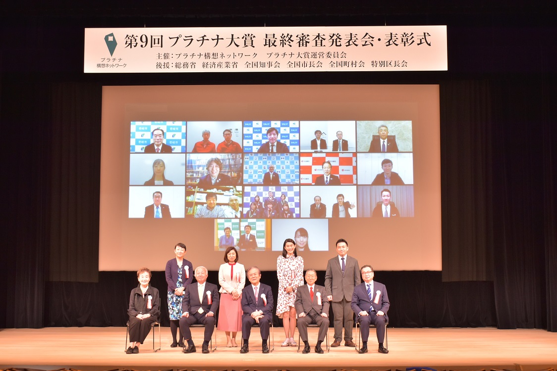 舞台上の審査員、スクリーン上の受賞者が写った表彰式会場の写真